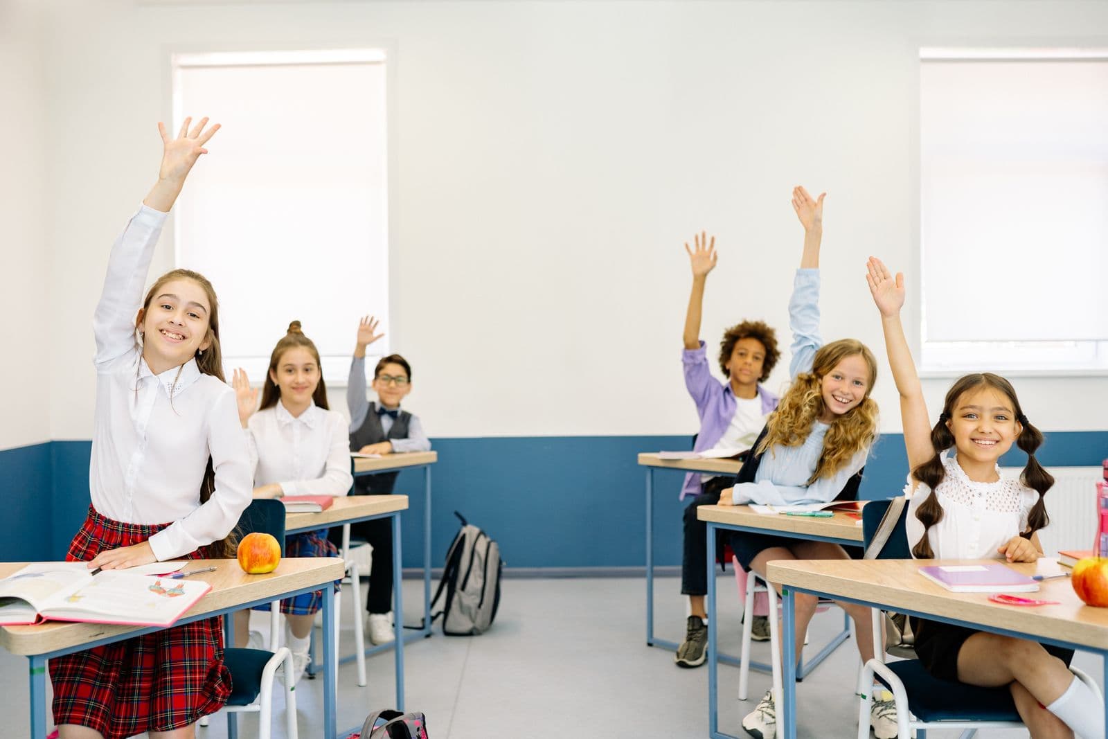 Elevi în bănci școlare care ridică mâna în timpul orei